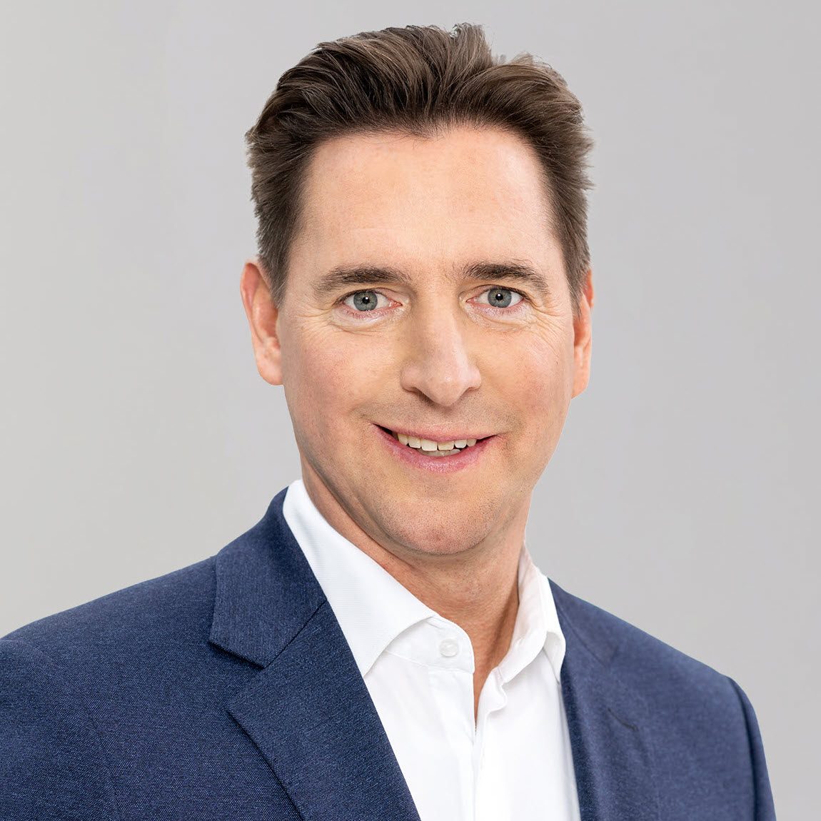 The image shows a person wearing a dark blue suit jacket and a white shirt.